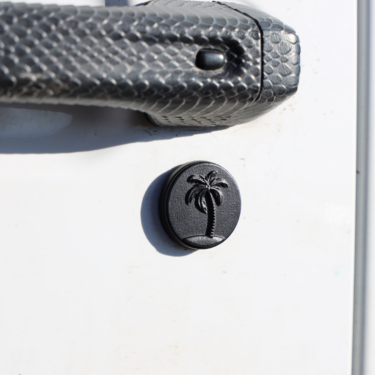A black keyhole trim cover with a palm tree design on a vehicle door.